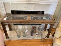 Full frontal view of wood sofa table with glass insets on top, showing wear in finish and decorative detailing on corners.