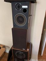 Stacked view of three speakers showing front speaker panels and wood finish on one speaker.