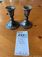 Two sterling weighted candle holders placed on a wooden table with a MaxSold lot tag showing lot number 222 and note 'Sterling Candle Holders'.