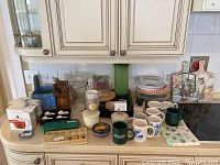 Wide view of countertop displaying Bodum mini teapot, assorted coffee cups, Tervis tumbler, brass doorbell, and multiple kitchen items