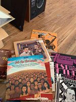 Photo showing a group of vinyl albums including 'We Are The World', Happy Birthday, and other artist albums on a wooden floor.
