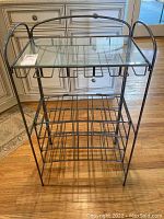 Front view of a metal wine rack with a clear glass top shelf, showing slots for wine bottles below.