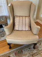 Front view of the beige upholstered wing back chair with striped cushion placed on the seat.