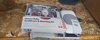Photo showing deluxe baby healthcare and grooming kit in a clear plastic case with various infant grooming tools, packaged white baby wipe holder, and baby backseat mirror.
