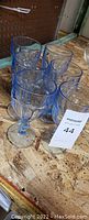 Photo showing six blue tinted goblet glasses arranged on a wooden board surface.