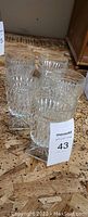 Four clear glass drinking glasses with a cut crystal pattern sitting on a wooden surface, tags included.