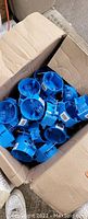 Open cardboard box filled with multiple blue round plastic electrical junction boxes, showing the inside of the box and many individual boxes piled together.