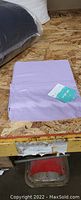 Photo of folded purple twin bed sheets with packaging tag on a wooden surface.
