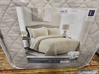 Photo of quilt packaging showing the Ava Diamond oversized king 3-piece cotton quilt set by Lush Decor in off-white diamond quilted pattern.