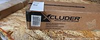 Closed cardboard box with Xcluder branding and pest defense label, featuring measurements and condition sticker.