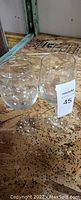 Photo of two clear used wine glasses placed on a wooden surface with a MaxSold tag showing number 45.