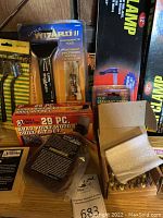 Wide view of the lot showing packaged metal detector, drill bit sets, lashing straps, and clamps.