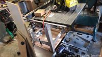 Craftsman 12 inch square table saw with metal frame, retractable roller base, and saw blade insert visible. Used for wood cutting.