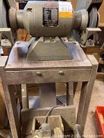 Full view of the bench grinder mounted on a metal stand, showing the grinding wheels and frame.