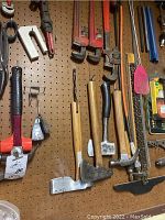 Photo showing various axes, pipe wrenches, and hammers hanging on pegboard.
