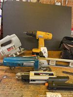 Photo showing assorted tools including yellow cordless drill, white jigsaw, blue angle grinder, PAMFast screw system, and metal level on a wooden table
