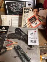 Photo showing NAPA Balkamp inductive timing light box with battery clips and inductive hook-up clamp, instruction manuals, and Actron Dwell/Tach model 612 box held by a person.