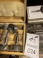 Wooden case partially open showing five Forstner bits wrapped in plastic under foam lid