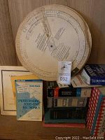 Photo showing vintage circular spring slide rule with accompanying technical books on solid-state electronics and hazardous materials.