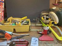 Various garden hose fittings, nozzles, pruning shears, hand pliers and a red garden sprinkler placed on a workbench.