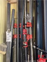 Metal pipe clamps with red clamping parts and long black pipes stored together.