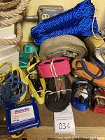 Photo showing a variety of ratchet straps, blue synthetic rope, beige natural fiber rope, some cords, and one of the blue plastic wall mount storage bins.