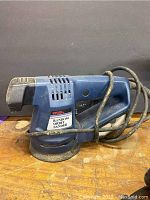 Blue Ryobi random orbit sander showing the side profile with cord wrapped