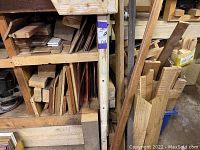 Wide view showing assorted scrap wood pieces including lumber, plywood, and wooden blocks arranged on shelving and floor