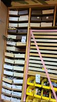 Front view of wooden storage drawer cabinet filled with labeled white trays.