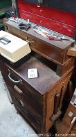 Wood cabinet with removable wooden chest on top, white tacklebox, and hand tools on lid