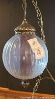 Full view of the hanging swag lamp showing the large ribbed glass globe and brass chain
