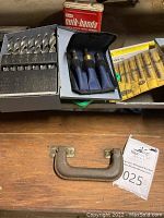 Inside metal case containing assorted large twist drill bits with sizing chart and small fabric pouch holding mortising chisels