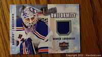 Front of the trading card showing Henrik Lundqvist in goalie gear and a blue fabric swatch from his New York Rangers jersey.