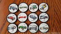 Top view of all 12 round Jello picture wheels laid out on a wooden surface, showing colorful illustrations of vintage cars and text with car brands and years.