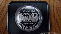 Obverse side of 1974 Canadian silver dollar showing Winnipeg Centennial design with 'WINNIPEG 100' and city skyline.