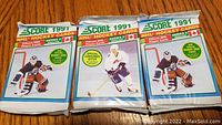 Photo of three unopened 1991 Score Series 2 NHL hockey card packs, showing front of each sealed pack with player images and promotional stickers.