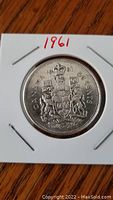 Front side of the 1961 Canadian 50 cent silver coin showing the Canadian Coat of Arms with intricate detailing, mounted in a protective holder.