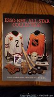 Front cover of the Esso NHL All-Star Collection sticker book showing hockey jerseys, gloves, sticks, pucks and goalie mask.