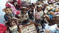 Close-up photo of several Boyd's Bears vintage figurines sitting with a sign reading 'Boyds Bears and Friends'. Bears are in various outfits, hats, dresses, and holding accessories