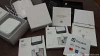 Photo of multiple Square Readers with packaging and manuals on a table, showing boxes of Square magstripe reader for iPhone/iPad, cables, and instruction materials.