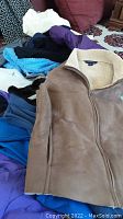 Photo showing collection of jackets and sweaters including tan suede jacket with shearling collar, blue fleece, purple and white sweaters, mostly unworn condition