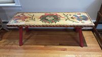 Top view showing full folk art painted design on the bench including flower, wreath with bow, and a traditional figure.