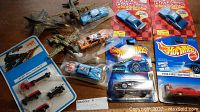 Top-down view of several die-cast toy cars including three Richard Petty #43 Hot Wheels and several fighter planes along with other collectible vehicles, some still in original packaging.