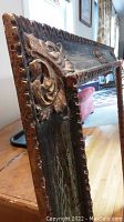 Close angled photo showing detailed floral and scroll carved wood decoration on mirror frame with distressed finish.