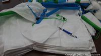 Multiple white mesh nylon bags with blue and green drawstring closures laid out with a pen for scale, showing different bag sizes.
