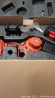 Top view of mini chain saw and accessories in foam packaging inside box.