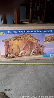 Box showing the full image of the 16 piece wooden nativity crèche and accessory set including the display base and accessories.