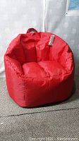 Red beanbag chair displayed from slight side angle showing shape, fabric, and handle on top.