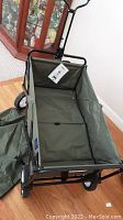 Front angle of army green folding wagon showing spacious fabric body, handle with grip, and metal frame.