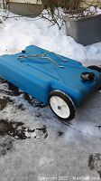 Blue plastic portable RV waste tank with two wheels and metal handle on snowy ground.